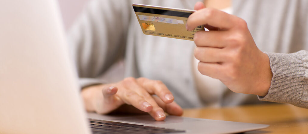 female hand holding a credit card in front of a laptop